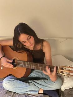 a woman sitting on top of a bed holding an ukulele and playing the guitar