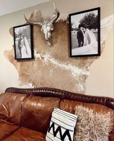 a brown leather couch sitting next to two framed pictures on the side of a wall