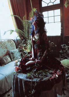 a woman sitting on top of a table in front of a window next to a plant