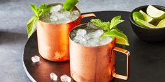 two copper mugs filled with ice and mint garnishes on a black tray