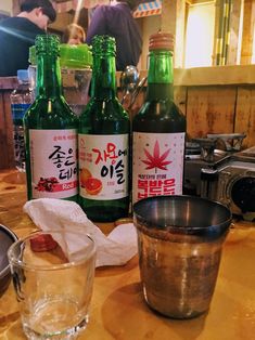 three bottles of alcohol sitting on top of a wooden table next to a glass cup