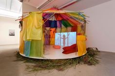 there is a colorful tent in the middle of an empty room with grass on the floor