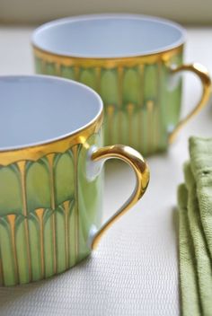 two green and gold coffee cups sitting on top of a table