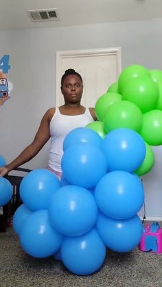 a woman standing next to a bunch of blue and green balloons in front of her