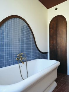 a bath tub sitting next to a wooden door in a room with blue tiles on the walls