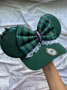 a person's hand wearing a green and black hat with a large bow