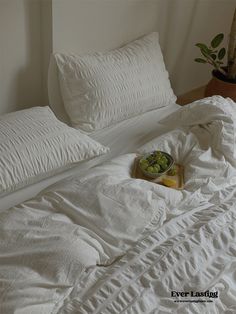 an unmade bed with two pillows and a bowl of fruit on the pillowcase