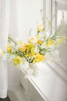 a white vase filled with yellow and white flowers on top of a window sill