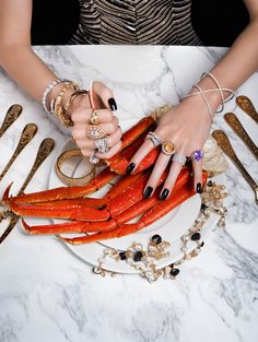 a woman is holding lobsters on a plate with gold rings and bracelets around her