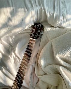 an electric guitar laying on top of a white sheet covered bed in the sun with its strings still attached