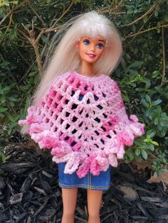 a doll with blonde hair wearing a pink crocheted ponchy shawl