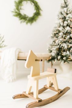 a wooden rocking horse sitting next to a christmas tree in a room with white walls