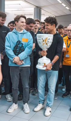 two men holding up a trophy in front of a group of people standing behind them