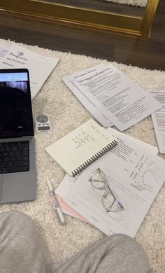 an open laptop computer sitting on top of a pile of papers next to a pair of glasses