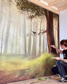 a woman is painting a mural on the wall in an art studio with trees and birds