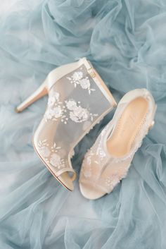 a pair of wedding shoes on top of a blue cloth covered bed sheet with white flowers