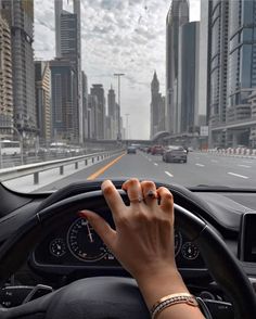 a person driving a car with their hand on the steering wheel, in front of some tall buildings