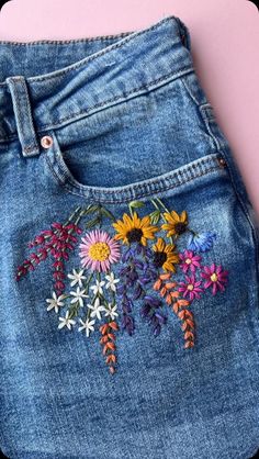 a pair of jeans with embroidered flowers on the back and side, sitting on a pink surface