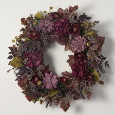 a wreath with purple flowers and leaves hanging on the wall next to a white wall