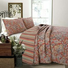 a bed covered in a colorful quilt next to a window with potted plants on it