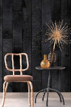 two chairs and a table in front of a wooden wall with a vase on it