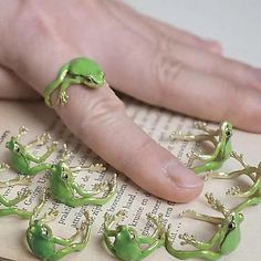 a person's hand is shown with green frog rings on top of an open book