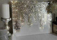 a candle and some white flowers on a shelf next to a wall covered in glitter