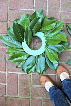 a person standing in front of a green wreath on the ground with leaves around it