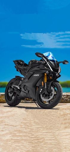 a black motorcycle parked on top of a sandy beach next to the ocean with blue skies in the background