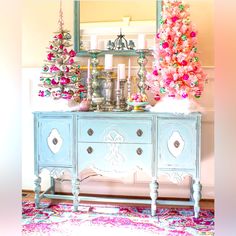 a blue dresser with pink and green ornaments on it's sideboard next to a christmas tree