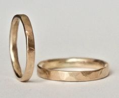 two gold wedding rings sitting next to each other on a white surface with one ring in the foreground