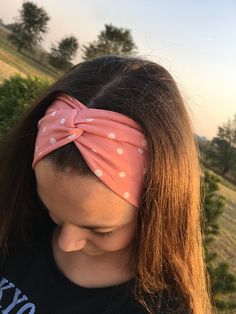 a woman with long hair wearing a pink polka dot headband and looking down at the ground