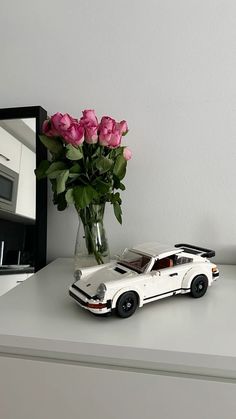 a white toy car sitting on top of a counter next to a vase with pink roses