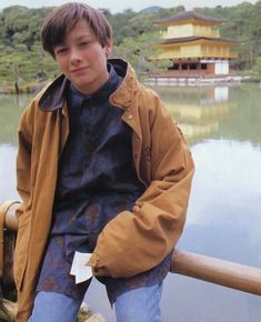 a young man sitting on the edge of a railing next to a body of water