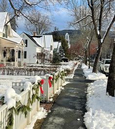 a street lined with houses covered in snow next to trees and christmas wreaths on the fence