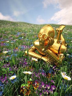 a gold statue laying on top of a lush green field filled with purple and white flowers