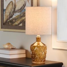 a lamp sitting on top of a wooden table next to a book and a painting