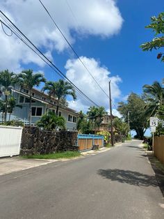 an empty street with houses and palm trees on both sides, in front of a blue sky