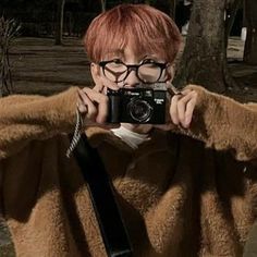 a woman taking a selfie with a camera in front of her, wearing glasses and a fur coat