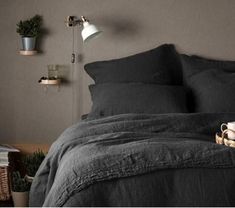 a bed with dark gray linens and pillows in a room that has potted plants on the wall