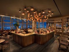 a restaurant with many tables and chairs in front of large windows overlooking the city at night