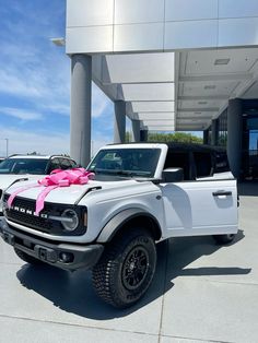 a white truck with a pink bow on the hood parked in front of a building