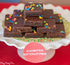 chocolate brownies with sprinkles are on a cake platter that says cosmic brownies