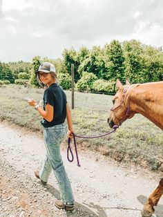 a woman walking a horse down a dirt road