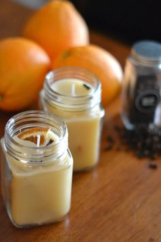 two jars filled with candles sitting on top of a wooden table next to oranges