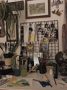 a cluttered desk with various office supplies and pictures on the wall above it,