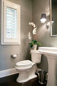 a white toilet sitting next to a sink in a bathroom under a window with shutters