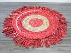 a round rug with fringes on top of a wooden floor next to a wall