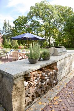 an outdoor grill made out of firewood and bricks with an umbrella in the background