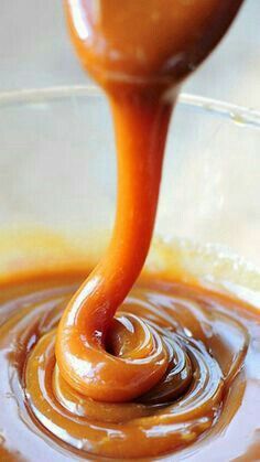 an orange sauce being poured into a glass bowl with caramel colored liquid in it